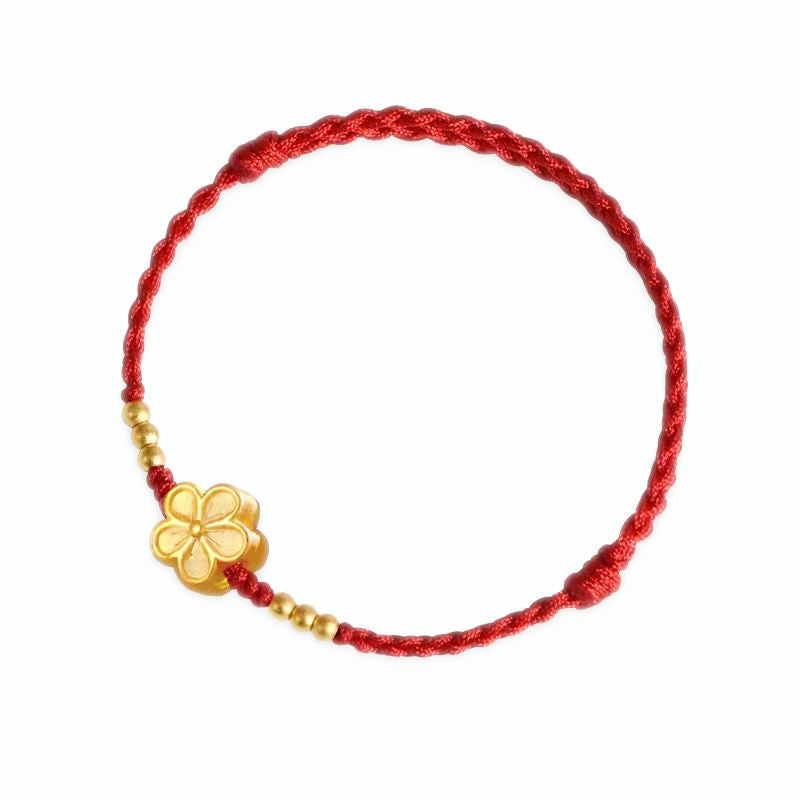 Close-up of a red woven bracelet with a gold flower charm worn on a wrist