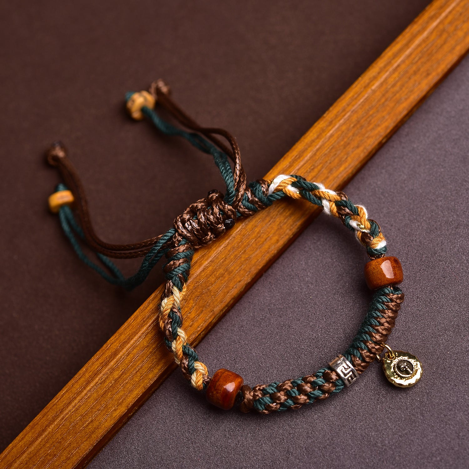 Close up of a multi-colored braided cord bracelet with wooden beads and a gold charm