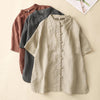 Three folded cotton linen shirts in beige, grey and brown showing the stand collar and button detail
