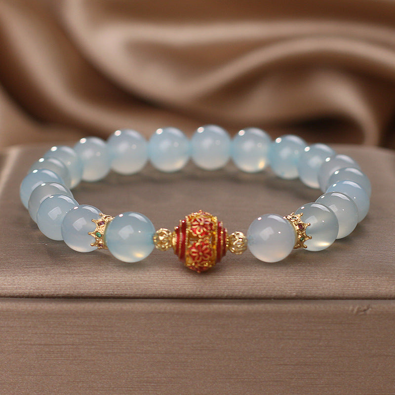 Sky blue chalcedony bead bracelet with a central red and gold charm resting on fabric