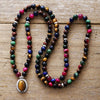 Long string of colorful tiger eye beads with an oval pendant resting on wood