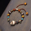 Hand-woven bracelet with bone skull bead and colorful accents on a dark wood surface