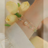 Close up of a gold plated copper bracelet with green jade beads and a white flower charm on a wrist