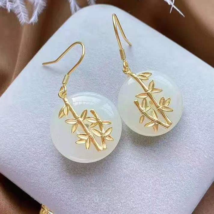 Pair of white jade earrings with gold bamboo accents on a display cushion