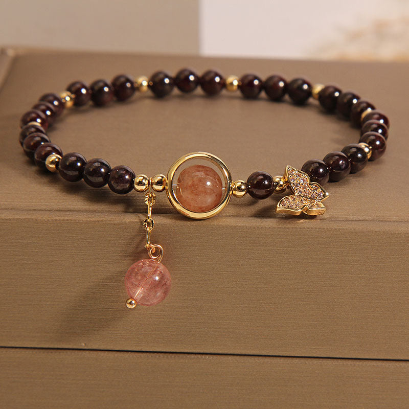 Close up of garnet beaded bracelet with gold butterfly charm and pink stone pendant