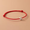 Close up view of a red woven cord bracelet with a silver four leaf clover charm