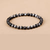 A hand holding a bracelet made of round black silver obsidian beads