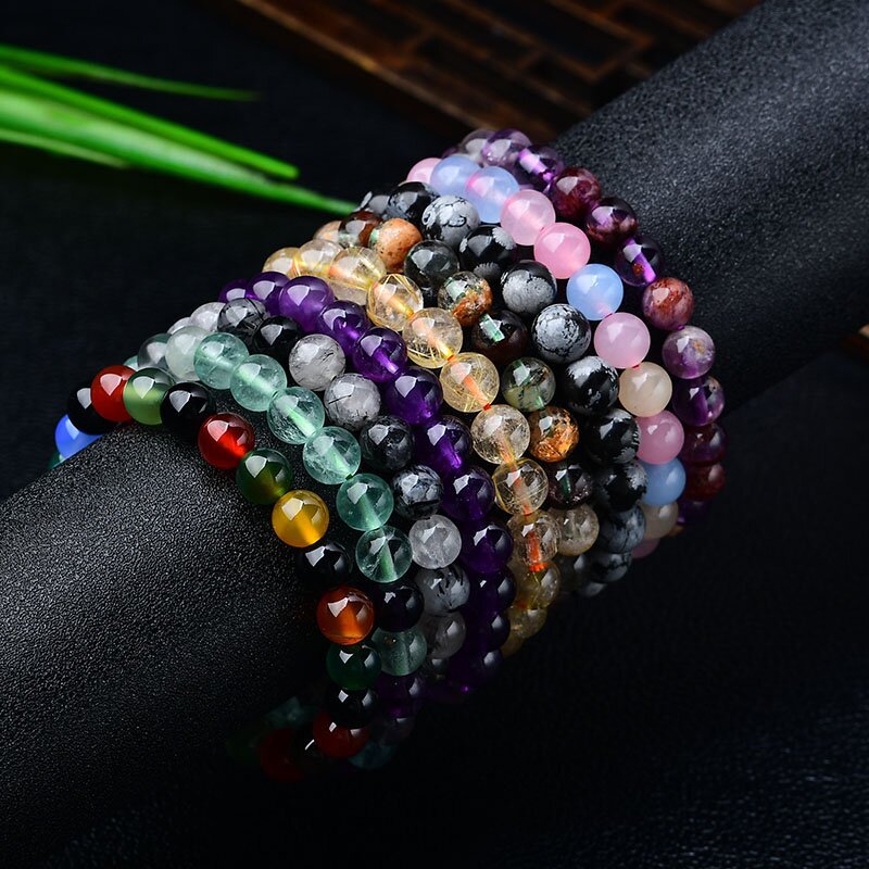 A wrist stacked with various colorful natural crystal bracelets including purple, green, and yellow stones.