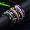A wrist stacked with various colorful natural crystal bracelets including purple, green, and yellow stones.