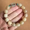 Hand holding a light brown yak horn bead bracelet with a silver-tone rectangular charm
