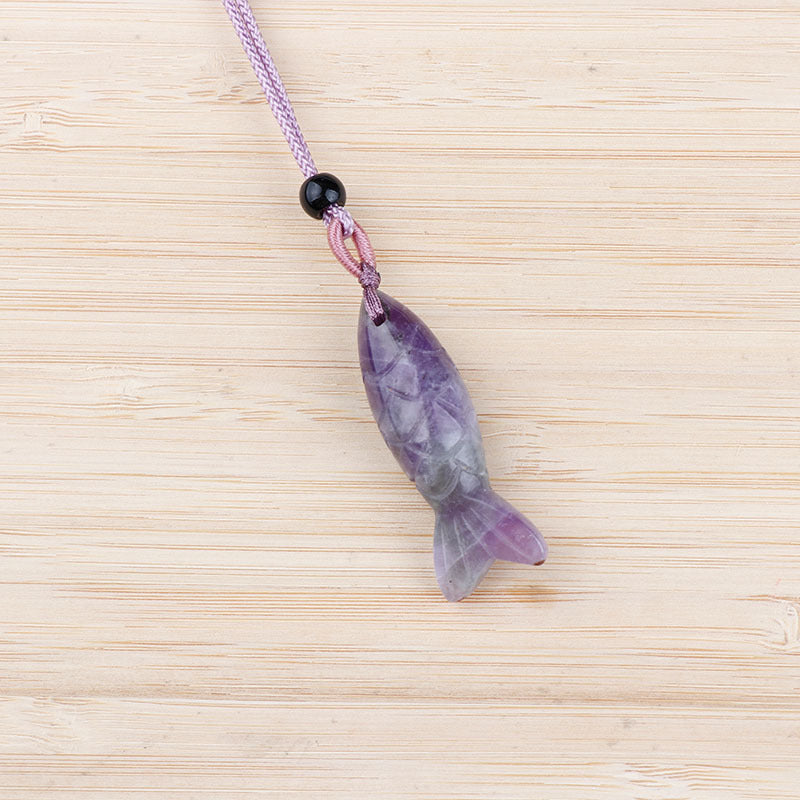 Close up of a purple carved amethyst fish pendant on a light purple cord