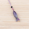 Close up of a purple carved amethyst fish pendant on a light purple cord