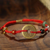 Close-up of a red string bracelet featuring a central copper coin charm and small accent beads on a wooden surface