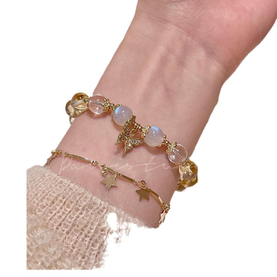 Close up of a wrist wearing a gold tone bracelet with yellow citrine and white moonstone beads plus a butterfly charm