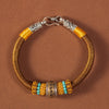 Close up of a red braided bracelet with gold and silver charms on a wrist