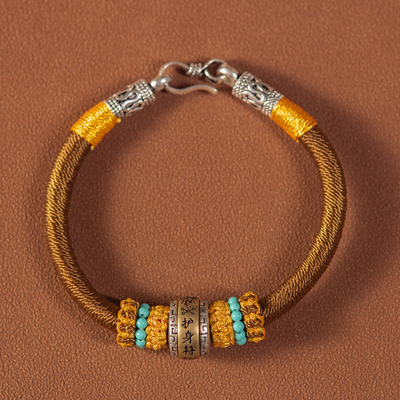 Close up of a red braided bracelet with gold and silver charms on a wrist