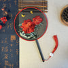 Close up of a black round hand fan with red peony embroidery and a red tassel