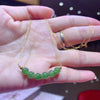 Hand holding a delicate gold chain necklace with seven round green jade beads