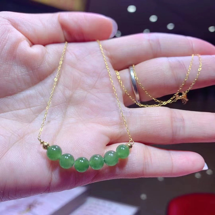 Hand holding a delicate gold chain necklace with seven round green jade beads