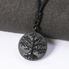 Close-up of a round black obsidian pendant with a carved tree design on a black cord