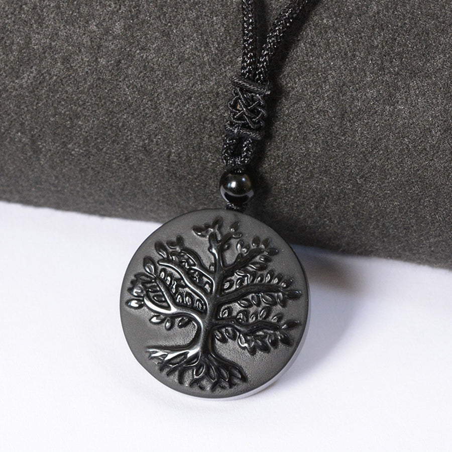 Close-up of a round black obsidian pendant with a carved tree design on a black cord