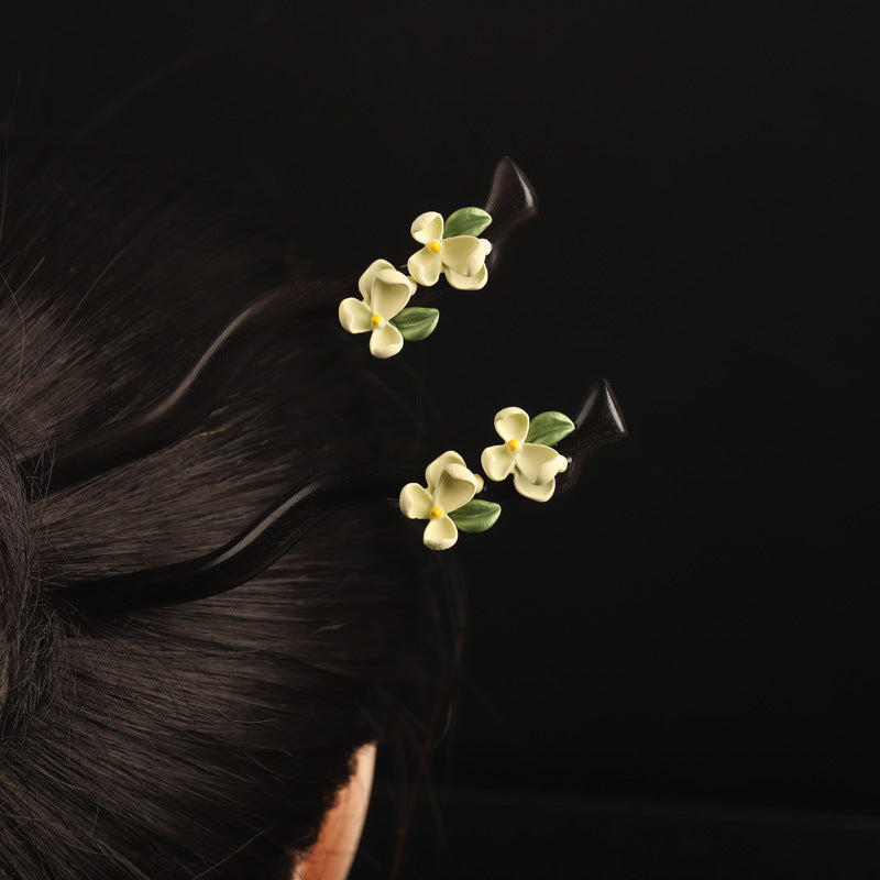 Close-up of a dark wood hairpin with small white gardenia flowers worn in black hair