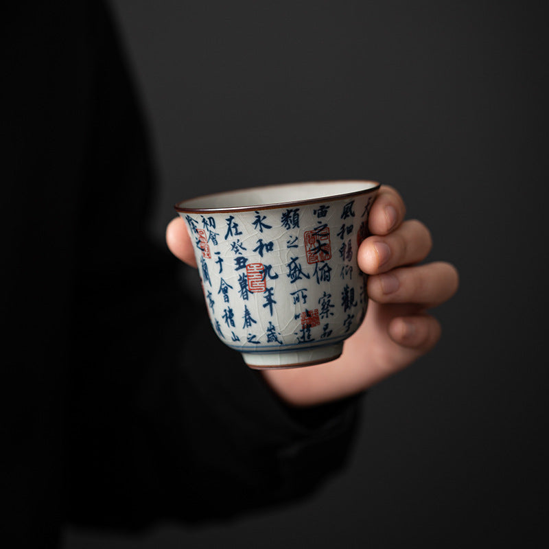 A hand holding a small blue and white porcelain teacup with Chinese calligraphy text.