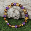 Close up of a beaded bracelet with purple amethyst and brown tiger eye stones on green grass
