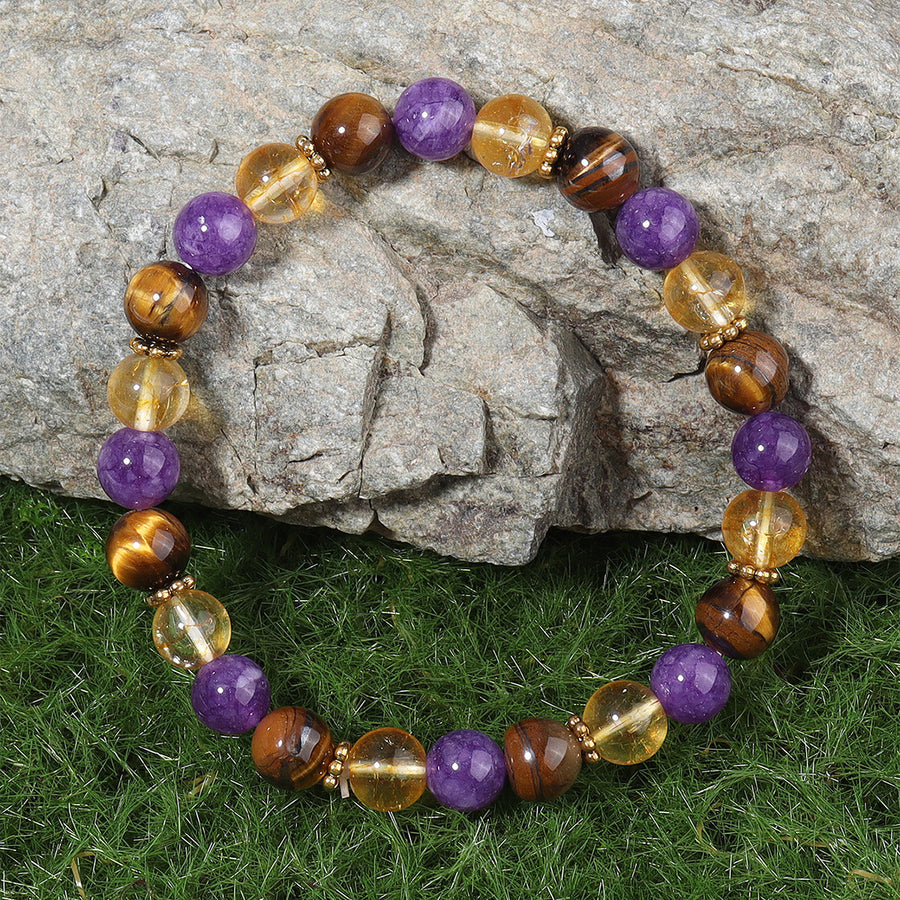 Close up of a beaded bracelet with purple amethyst and brown tiger eye stones on green grass