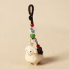 Close-up of a light-colored wooden sheep keychain with a braided brown cord and red, black, and green beads.