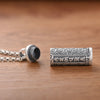 Antique silver cylindrical pendant with Tibetan script engraving lying on wood surface