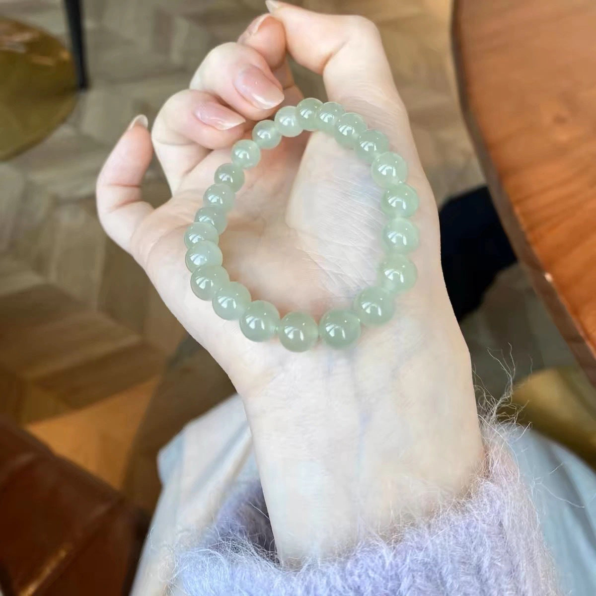 A hand holding a light green beaded jade bracelet against a soft background