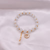 Close-up of a white cat's eye bead bracelet with a gold butterfly charm on a white cloth background.