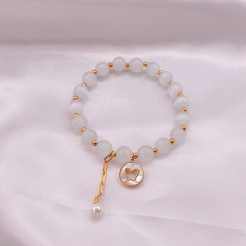 Close-up of a white cat's eye bead bracelet with a gold butterfly charm on a white cloth background.