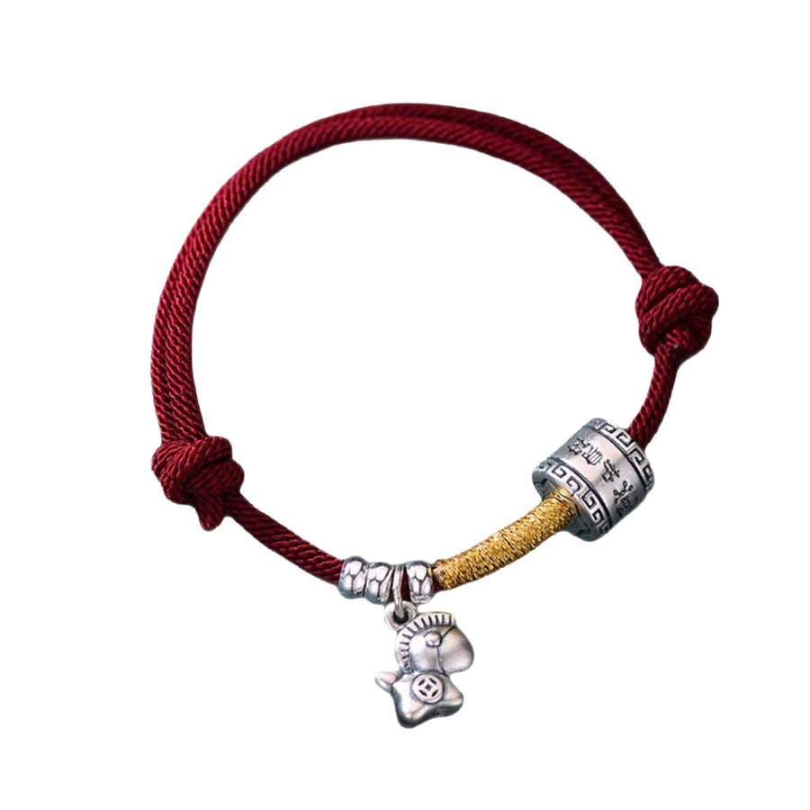 Close up of a red knotted bracelet with a silver horse charm and bead