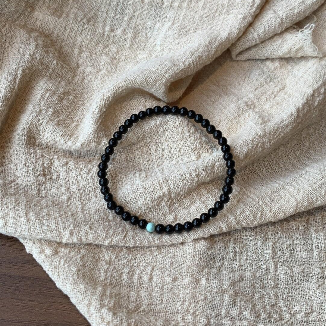 Black glass bead bracelet with one green bead on a linen cloth
