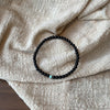 Black glass bead bracelet with one green bead on a linen cloth