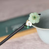 Close up of a wooden hair stick with green and white flower decorations