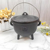 Small black cast iron cauldron with a lid and handle sitting on a marble surface.