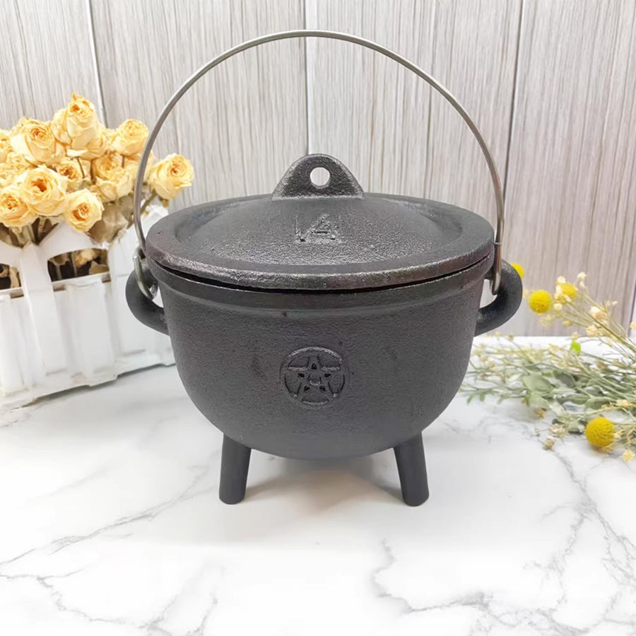 Small black cast iron cauldron with a lid and handle sitting on a marble surface.