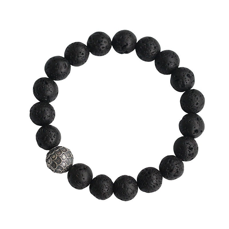 Close up of a black lava rock bracelet with one silver fish scale bead on a wrist