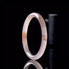 Close up of a translucent violet and beige Golden Silk Jade bangle standing upright on a black surface