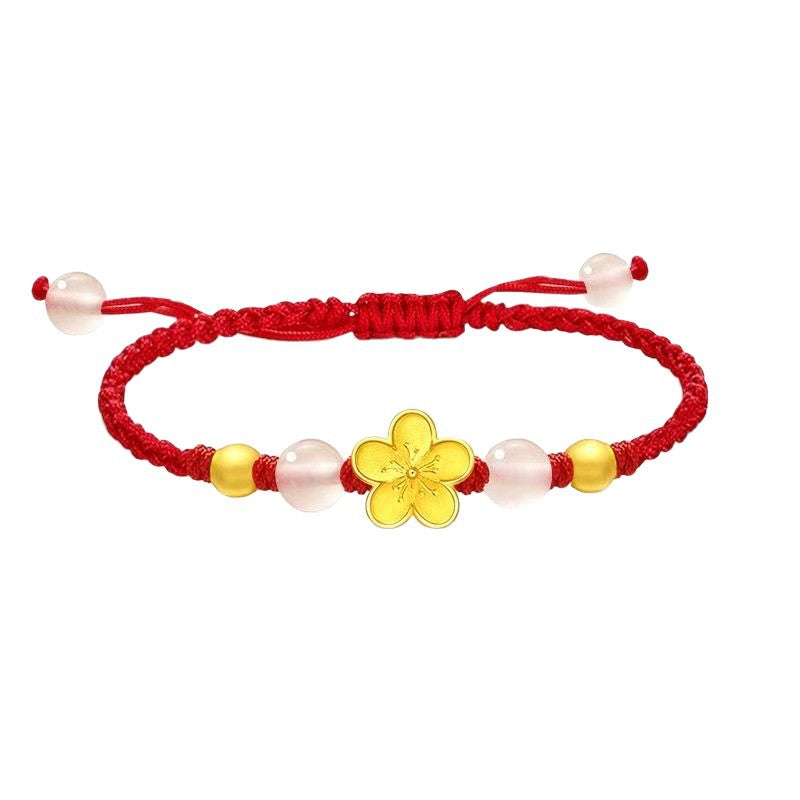 Close up of a wrist wearing a red string bracelet with a gold flower charm and pink beads
