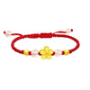 Close up of a wrist wearing a red string bracelet with a gold flower charm and pink beads