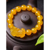 Close up of a yellow beaded bracelet with a Pixiu charm resting on a dark teapot lid