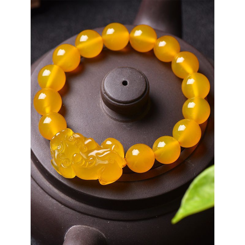 Close up of a yellow beaded bracelet with a Pixiu charm resting on a dark teapot lid