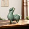 A green ceramic goat figurine sitting on a wooden table