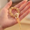 Hand holding a yellow jade wrist mala with white pearl accents and a hanging peace buckle charm