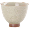 Close up of a cream colored ceramic cup with a honey glaze and raised floral relief design