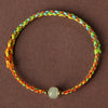 A close-up of a multi-colored braided rope bracelet with a single light green jade bead in the center.